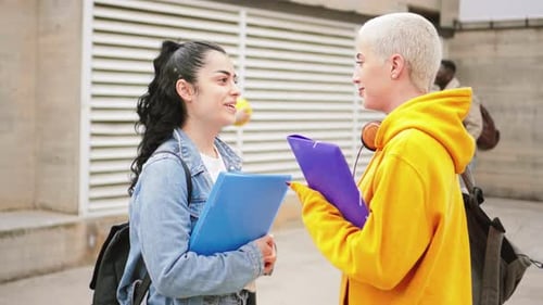 Two Young Gossip Girls Talking at the University Campus in the Background Two Multiethnic Teenagers