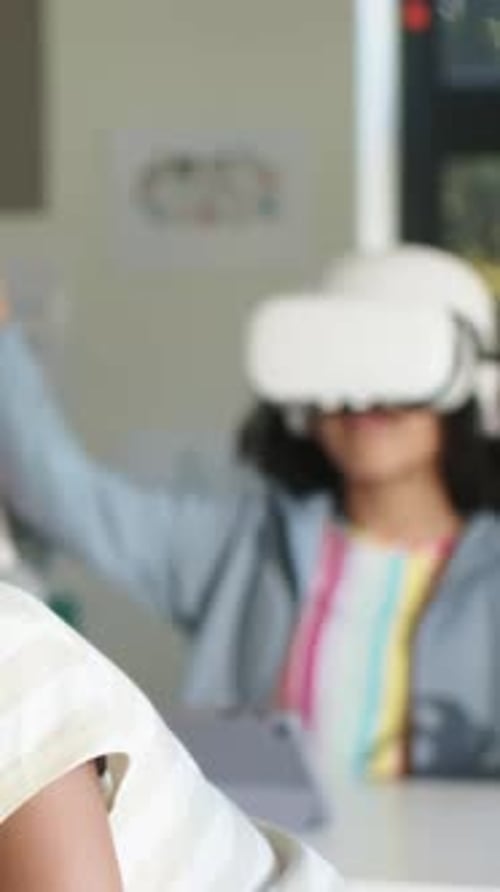 Lifting white VR headset, student in blue hoodie gesturing at school desk using tablet for lesson