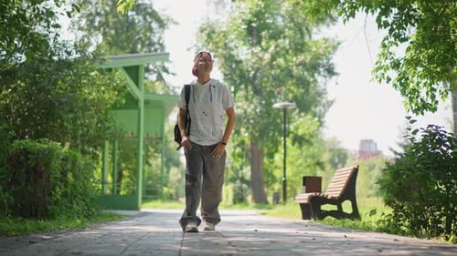 Man Strolling Along Shaded Walkway with Backpack Glancing Upward at Trees Slow Pace Bench and Green