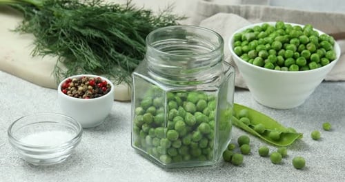 Putting fresh green peas into pickling jar on white table, closeup