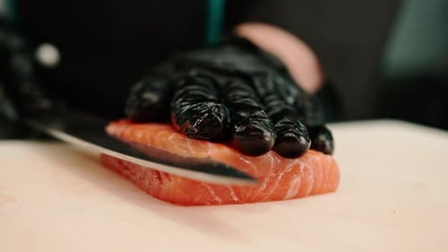 Close-up of a sushi chef cutting a salmon fillet with a knife while preparing sushi in the kitchen