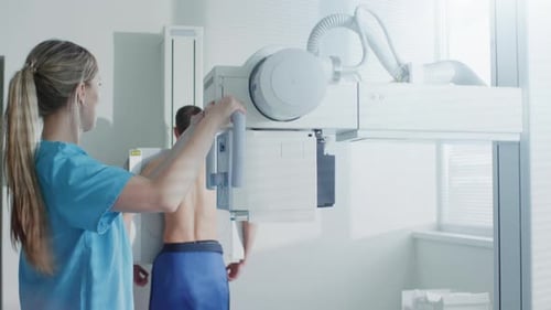 Im Krankenhaus steht ein Mann mit dem Gesicht an der Wand, während der Medizintechniker das Röntgengerät einstellt