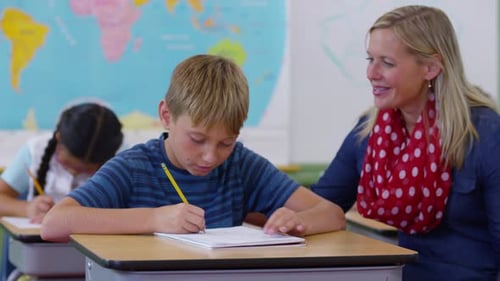 Teacher assists elementary school student with writing assignment in classroom