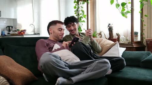 Gay male couple laughing while using a smartphone at home