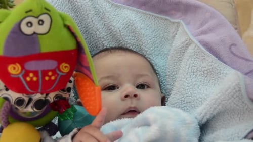 cute tree months old baby boy trying to eat blanket while sitting in baby bouncer with bunny toy