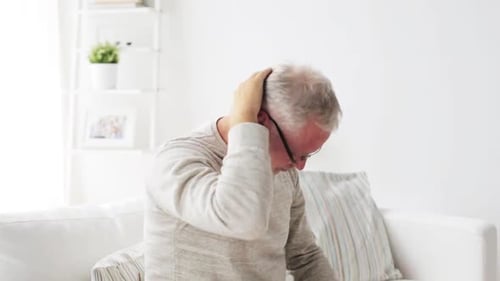 Mature man experiencing headache and neck pain at home