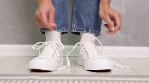 Woman tying shoelaces of white sneakers indoors, closeup