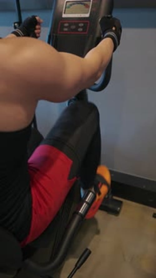 Muscular man doing cardio on stationary bike in modern gym