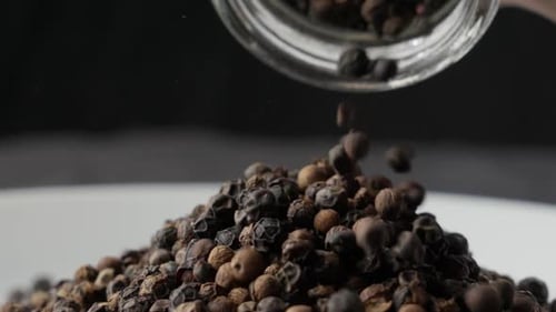 Black Peppercorns Pouring from Glass Jar in Studio