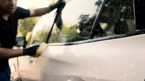Close up of a male washing a car wearing a black gloves with shampoo and sponge