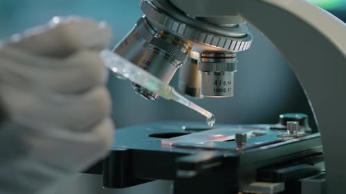 Hand of Scientist Adding Drop of Liquid to Specimen under Microscope