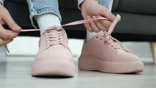Woman tying shoelace of beige sneaker indoors, closeup