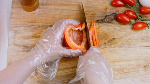 Front View of the Young Chef Cut Thin Slices of a Piece of Red Pepper with a Knife on the Cutting