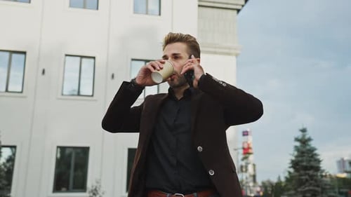 Man Talking on the Phone While Enjoying a Coffee Outside a Modern Building