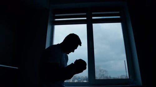 Silhouette of Father Holding Newborn Infant by Window