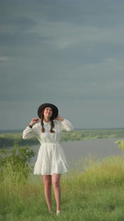 Woman Stands in Field Wearing Hat and White Dress