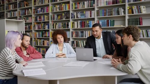 Confident Male Professor Working with a Group of University Graduate Students in the Library Campus