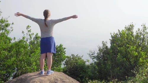 Young woman raising hands on top of mountain