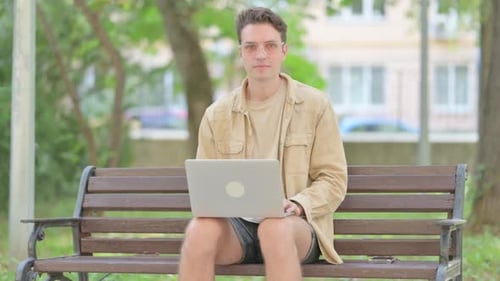 Man Working On Laptop Smiling On Park Bench