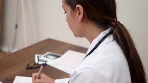 Female Doctor Works on Diagnosis Examining Patient Ultrasound Examination Images and Making Notes