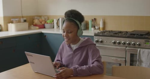 Teen using Laptop with Headphones in Kitchen