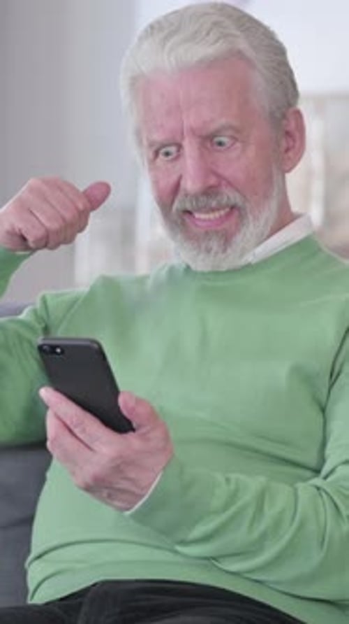 Senior Man Excited While Using Smartphone Indoors