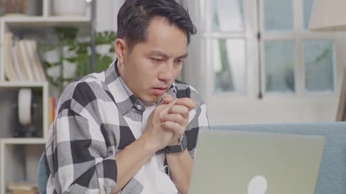 Close Up Of Asian Man With Blanket Trying To Get Warm While Lying On Sofa Works On A Laptop
