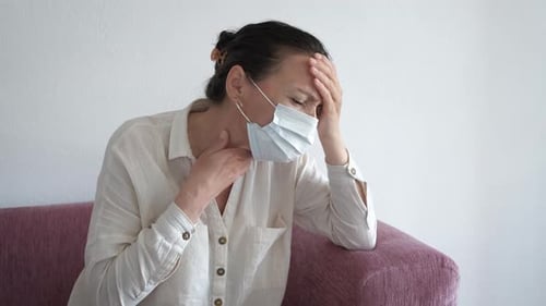 Woman Touching Head and Throat Wearing Mask