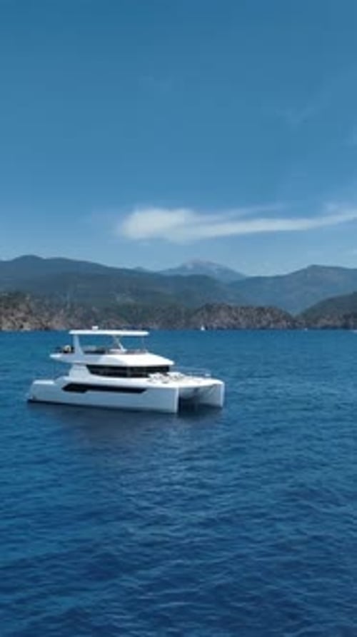 Moderno catamarán blanco que navega en un mar azul tranquilo con una costa montañosa