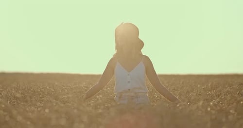 Beautiful Girl in a Hat Walks Through a Wheat Field at Dawn