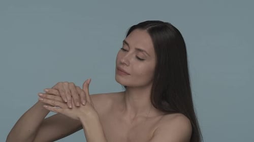 A Woman Applies Rubs the Cream Into the Skin of Her Hands on a Blue Background A Seminude Woman