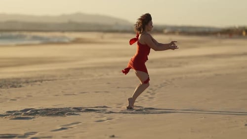Woman Dancing Barefoot on Sandy Beach at Sunset