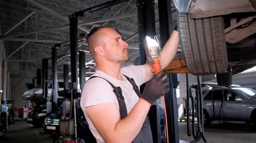 Man Fixing Car in Garage Using Auto Parts and Tools
