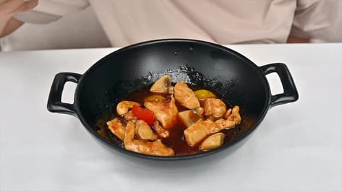 Woman eating chicken with vegetables and sweet sauce in a black pan at a chinese restaurant