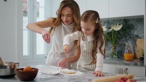Woman and girl sprinkle flour on pastry dough