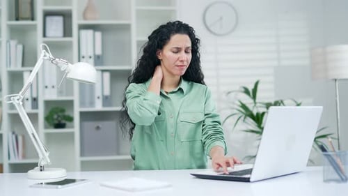 Woman Massaging Stiff Neck While Working at Desk