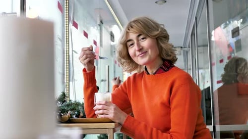 Beautiful Woman Drinks Coffee From a Transparent Mug in a Cafe
