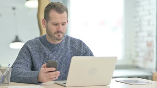 Man Using Smartphone and Laptop in Office Setting