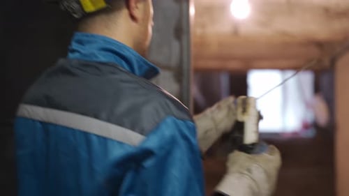 Professional Welder in Safety Suit and Protective Mask Comes Up to Welding Machine Takes Electrode