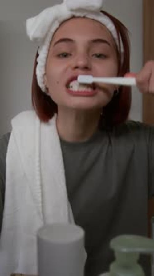 Young Woman Brushing Teeth in Bathroom Mirror