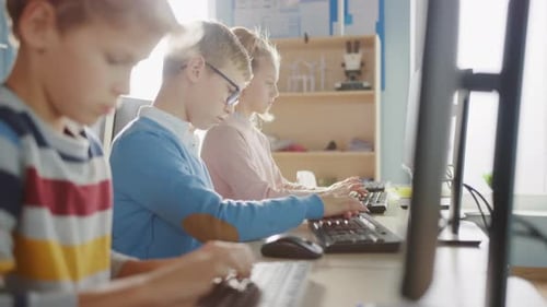 Elementary School Classroom: Portrait of a Smart Boy with Glasses Uses Personal Computer, Learning