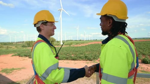 Intelligente Ingenieure mit Schutzhelm beim Händeschütteln im Feld elektrischer Turbinen