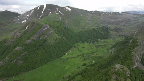 Flying over beautiful green mountains. In the background, stone cliffs with snow are visible.