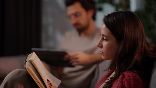 Side View of a Confident Brunette Girl in a Red Sweater Reading a Book While Sitting on the Sofa