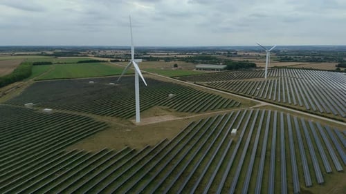 Wide drone shot of clean energy infrastructure including solar and wind farm producing electricity
