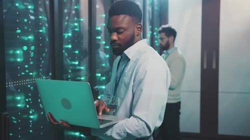 A Focused Man Works on a Laptop in a Hightech Server Room