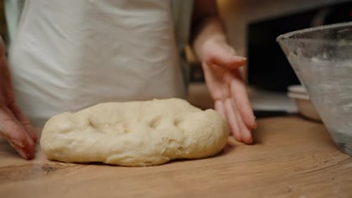 Hands Pressing and Folding Dough on a Wooden Surface, Final Preparation Before Baking, Ensuring