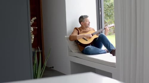 Man Plays Guitar by Sunny Window at Home