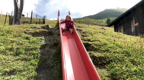 Girl Slides Down Slide in Mountainous Landscape