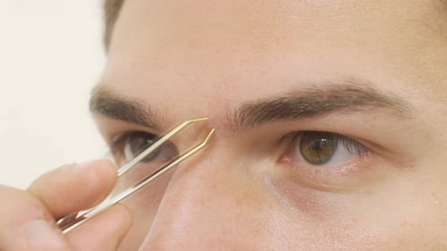 Man Plucking Eyebrow Hair with Tweezers Close Up